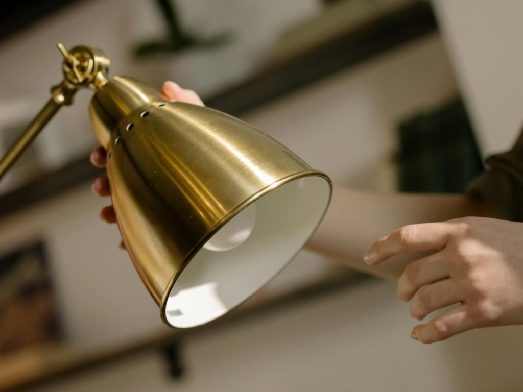 Close-up of a brass desk lamp being adjusted by hand in a cozy home interior setting.