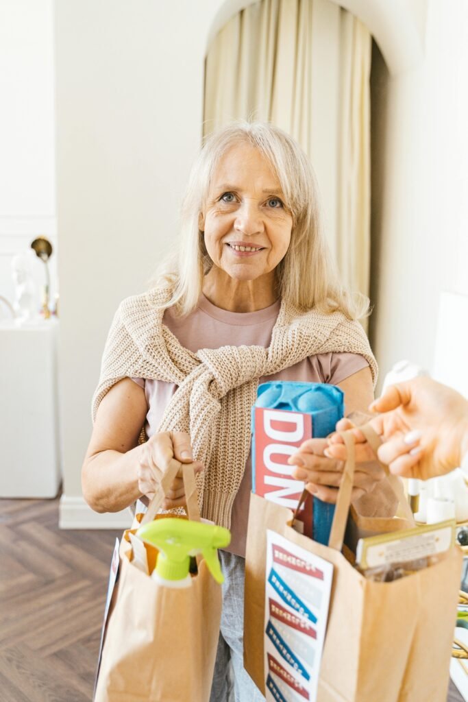 Happy elderly woman with groceries in paper bags, smiling indoors.